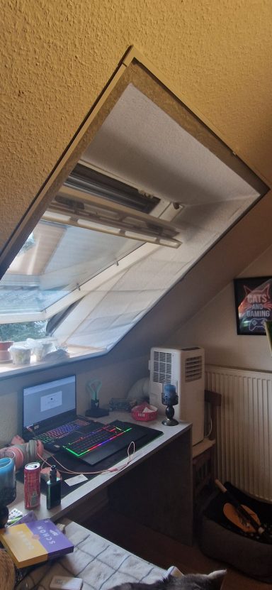 Arbeitsplatz unter einer Schräge mit Computer, Monitor, Fernseher und Spiegel.