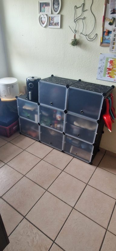 Ein Regal mit transparenten Kisten, das auf einem Fliesenboden steht.