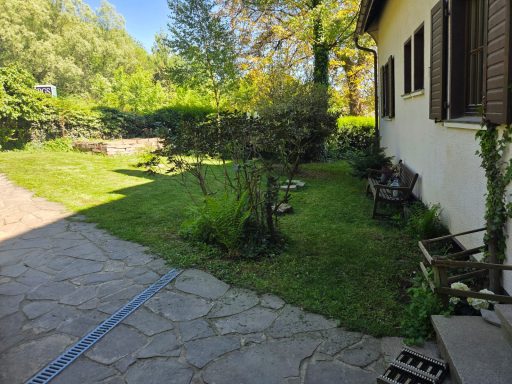 Garten mit Rasen, Bäumen und einem gepflasterten Weg neben einem Wohnhaus.